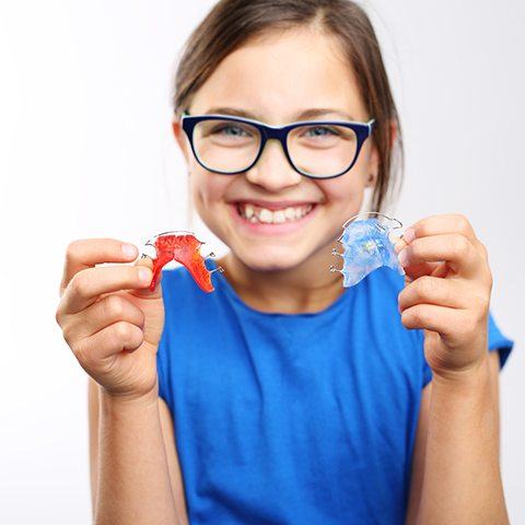 Young girl holding up red and blue removable retainers
