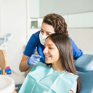 Teen orthodontic patient looking at her braces in hand mirror