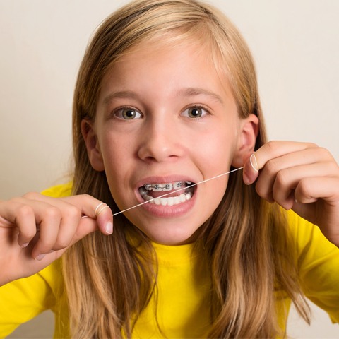 Yong girl with braces flossing to prevent orthodontic emergencies