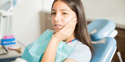 Young woman experiencing pain related to orthodontics holding her cheek
