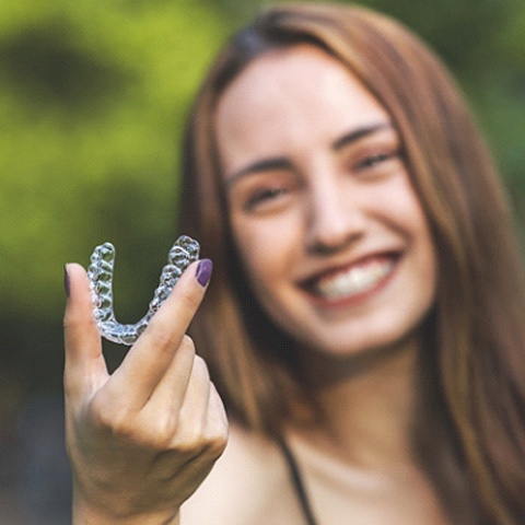 Happy woman holding her Invisalign® aligner in photo’s foreground