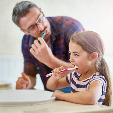 Father and daughter brushing teeth together