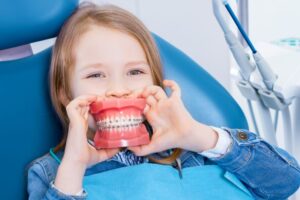 Child holding braces model in front of her mouth
